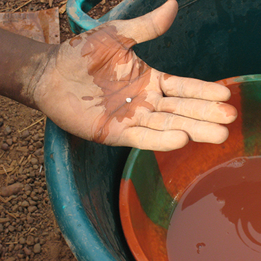 A miner’s hand holds a pebble-sized bit of mercury-covered gold ore over a bowl of water. The picture was taken at a small-scale gold mine in Senegal